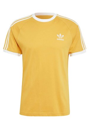 Camiseta amarilla de Adidas con cuello blanco, puños de las mangas, tres rayas en los hombros y el logo de Adidas en el lado izquierdo del pecho.