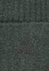 Próbka tekstury zielonej tkaniny z siatkowatym wzorem. Zawiera wytłoczony logo w ciemnej nitce. Miękka, puszysta powierzchnia.