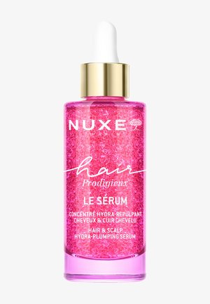 Roze NUXE haarserumfles met gouden druppeldop, bevat hydra-plumping concentraat voor haar- en hoofdhuidverzorging.