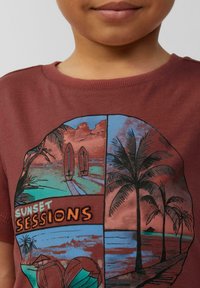 Bordowa koszulka z graficznym nadrukiem przedstawiającym palmy, deski surfingowe i morskie krajobrazy pod napisem "ZESTAWY ZACHODU SŁOŃCA". Materiał bawełniany.