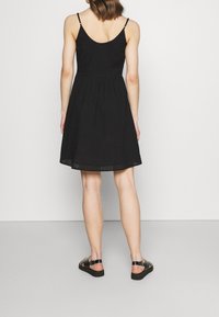 Vestido negro sin mangas con una tela texturizada, cintura fruncida y falda acampanada. Presenta un diseño con corte en el bajo.