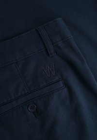 Navy blue pants featuring a textured fabric, with a visible button and a subtle "W" logo embroidered on the pocket.