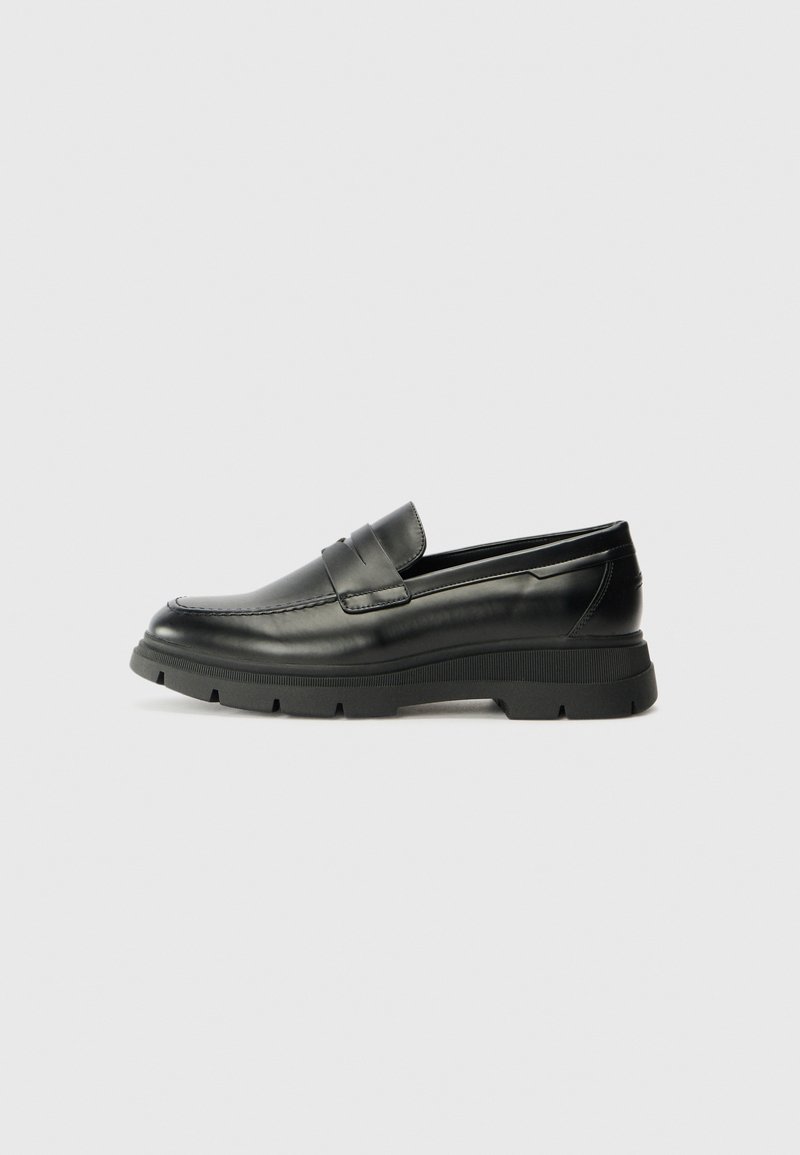 Black leather loafers with a rubber sole. The design features a stitched upper and a broad strap across the instep. Smooth texture, contemporary shape.