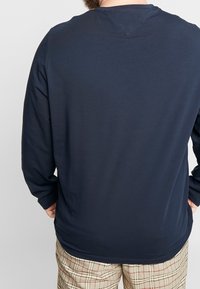 Granatowa koszula z długim rękawem, wykonana z miękkiego, elastycznego materiału. Prosty fason z okrągłym dekoltem i bez widocznych znaków firmowych. Krój typu template z delikatnym wycięciem u dołu.