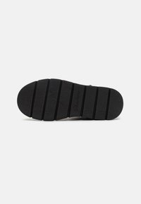 Semelle de chaussure en caoutchouc noir avec un motif floral texturé, un design segmenté et le nom de la marque "Skechers" en relief sur le côté.