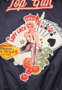 Marineblaues Sakko mit lebhaften gestickten Patches, darunter ein Pin-up-Mädchen, Spielkarten und Vegas-Themen-Symbole in kräftigen Farben.