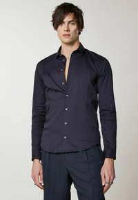 Camicia a maniche lunghe blu navy in tessuto liscio con colletto, abbottonatura frontale e vestibilità sartoriale. Presenta una leggera lucentezza e polsini.