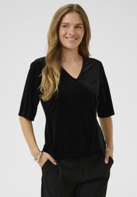 Top in velluto nero con scollatura a V e maniche corte; presenta una vestibilità comoda e una texture morbida; abbinato a pantaloni strutturati.