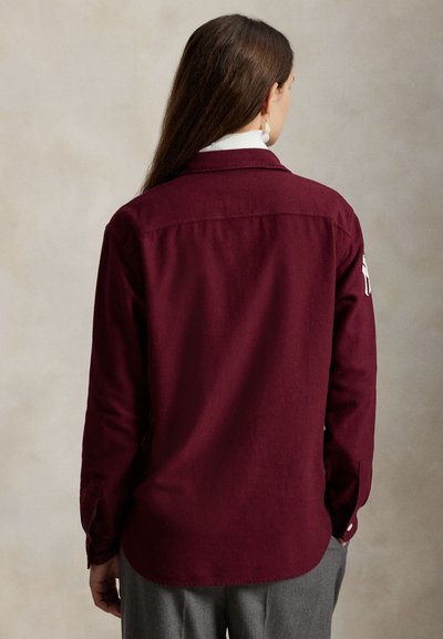 Καστόν μακρυμάνικο πουκάμισο με γιακά που κλείνει με κουμπιά και λεπτομέρειες στα μανίκια. Κατασκευασμένο από υφή υφάσματος, διαθέτει ραφή στην πλάτη.