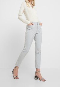 Top de manga larga color beige claro, pantalones grises ajustados y sandalias de tacón alto en blanco y negro a rayas, con una textura suave y un diseño ajustado.