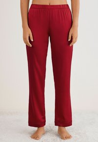 Rode satijnen pyjamabroek met een elastische tailleband, rechte pijpen en omgeslagen broekspijpen. Glad textuur zonder zichtbare patronen of accenten.