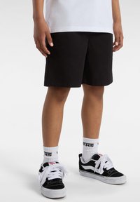 Pantaloni corti neri in cotone, con un design semplice e una consistenza liscia. Abbinati a sneakers nere Vans e calze bianche con logo.