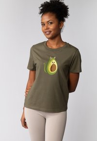 Olivegrünes Baumwoll-T-Shirt mit einem Cartoon-Avocado-Graphic, die Katzenohren und ein lächelndes Gesicht hat, kurzen Ärmeln und einem runden Ausschnitt.