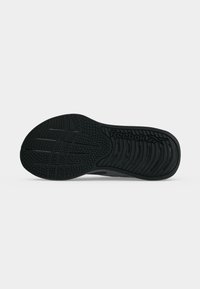 Μαύρη σόλα παπουτσιού Reebok με υφή στο πέλμα και το λογότυπο Reebok στην περιοχή της φτέρνας σε απλό ανοιχτό φόντο.