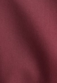 Bordeauxfarbener Stoff mit feiner Webstruktur und sanften Falten, die weiche Schatten und Highlights erzeugen.