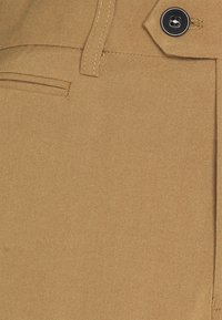 Béžové kalhoty z lehkého materiálu, s jemnou texturou, standardními kapsami a jedním černým knoflíkem jako ozdobou na pase.