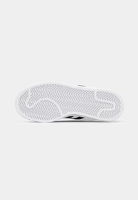 Sole of a sneaker with a white rubber base, featuring a herringbone tread pattern and a black stripe near the arch.