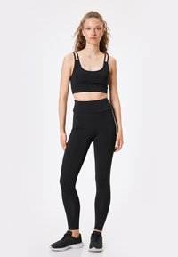 Zwart atletisch crop top met dunne bandjes, gecombineerd met hoge zwarte leggings. Beide gemaakt van rekbaar materiaal met een gladde textuur.