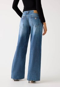 Jeans de denim azul de pierna ancha con un acabado desgastado, que cuentan con dos bolsillos traseros y una etiqueta de cuero con la marca por encima de la cinturilla.