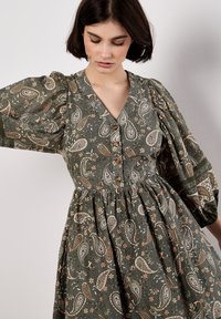 Vestido verde con estampado de paisley, mangas abullonadas, escote en pico y detalles de botones, que presenta acentos florales y una cintura fruncida.