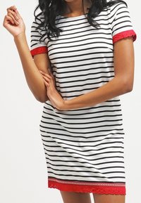 Robe rayée en blanc et noir, ornée de dentelle rouge sur les manches et l'ourlet. Tissu doux, manches courtes, coupe décontractée.