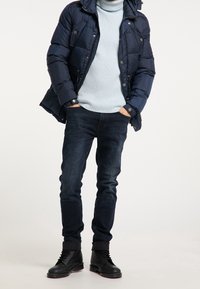 Granatowa kurtka puchowa z ukośnym pikowaniem, jasnoniebieski sweter z prążkowanym splotem, ciemne dżinsy, czarne sznurowane buty na solidnej podeszwie.