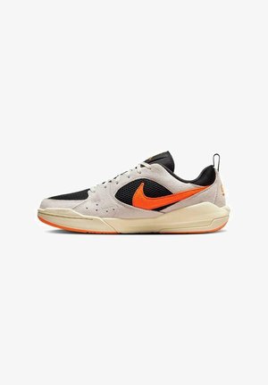 Zapatilla baja con ante beige, paneles de malla negra, logo Nike en naranja brillante y suela beige con detalles en naranja.