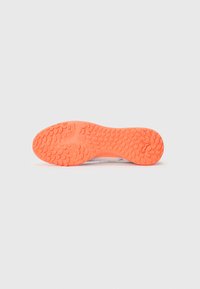 Semelle texturée orange vif d'une sneaker avec des motifs de grip ovales et un petit logo près du talon, présentée sur fond blanc.