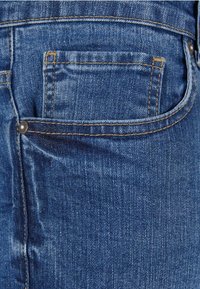 Traperice tamnoplave boje, s stražnjim džepom, vidljivim koncima u kontrastnoj žutoj boji i metalnom zakovicom.
