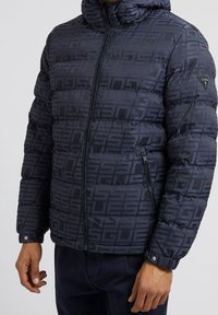 Navyblauwe gewatteerde jas met geometrisch patroon, ritssluiting, afneembare capuchon en zijzakken. Getextureerde stof met een gladde afwerking.