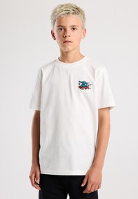 White cotton t-shirt featuring a colorful embroidered design of a blue figure on a skateboard. Short sleeves and a crew neckline.