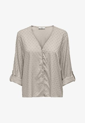 Blusa bege clara com decote em V, mangas três quartos, detalhes em botão e tecido texturizado com pequenos pontos elevados por todo o lado.