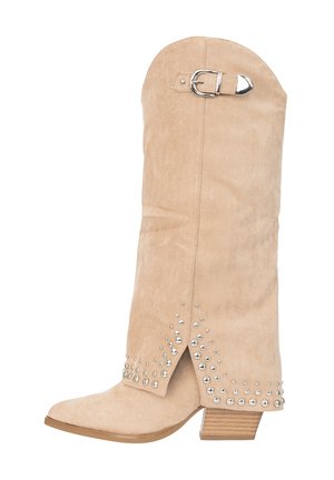 Beige suède laars tot halverwege de kuit met een houten blokhak, een zilveren gespsluiting bij de bovenzijde en zilveren studs langs de enkel en voorste opening.