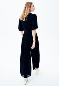 Mono de marina con plisado, mangas cortas y amplias, cintura ceñida y piernas acampanadas. Se lleva con tacones de plataforma de color claro.