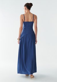 Tumši zils maksi kleita ar plānām siksnām, pieguļošu krūšu daļu un plūstošu svārku daļu. Kleitai ir rāvējslēdzējs muguras pusē un drapējumi pie vidukļa, radot slāņotu efektu.