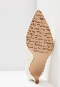 Chaussure à talon haut blanche avec une tige texturée, un bout pointu et une semelle marron portant un motif de marque répétée. Taille 37 indiquée sur la semelle.