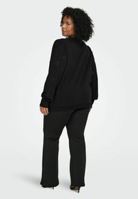 Črn pulover z izvezenimi cvetličnimi detajli na rokavih, kombiniran s črnimi hlačami. Mehka tekstura, sproščen kroj in dolžina do gležnjev.