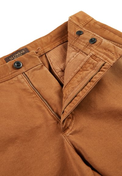 Bruine katoenen broek met ritssluiting en knoopsluiting. Zacht textuur met een gladde afwerking en een merklabel aan de binnenkant van de tailleband.