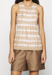Světle béžová bezrukávová halenka s bílým tie-dye vzorem, žebrovanou strukturou a kulatým výstřihem, spárovaná s hnědými šortkami.