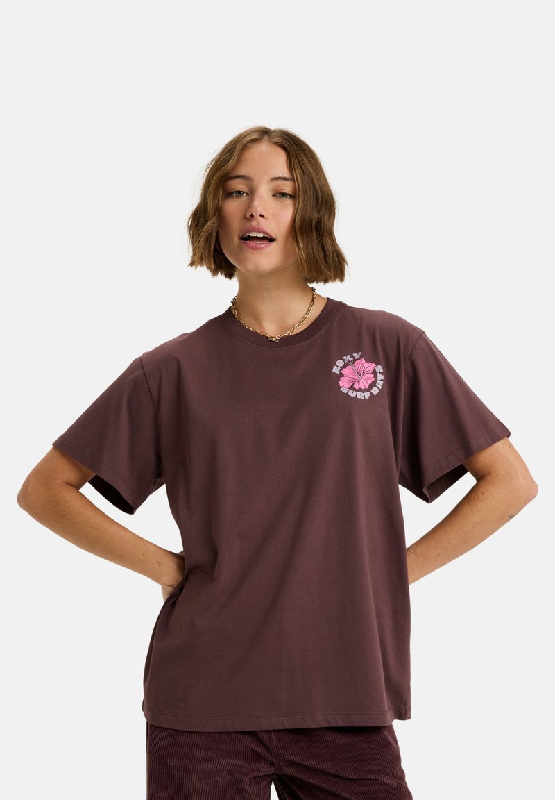 Bruine katoenen t-shirt met korte mouwen, met een roze bloemenafbeelding op de linkerborst. Rechte snit en zachte textuur.