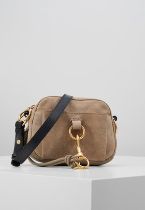 Bolso bandolera de ante en color marrón claro con una correa negra, que presenta un anillo y un cierre de herrajes en tono dorado. Superficie texturizada con una base lisa.