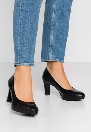 Sorte læder højhælede sko med rund tå og en glat overflade. Kombineret med lyse denim, der fremhæver en tætsiddende pasform ved anklen.