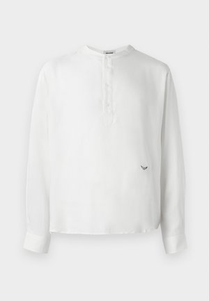 Hvit langermet skjorte laget av glatt stoff, med rund hals, knappestolpe og en liten brodert detalj ved kanten.