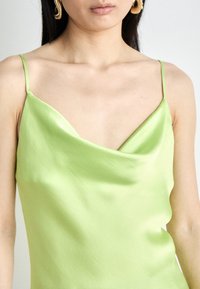 Satin-grüne Spaghettiträger-Camisole mit einem Cowl-Ausschnitt. Der Stoff hat eine glatte Textur, die das Licht dezent reflektiert.
