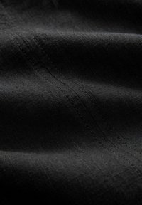 Gros plan sur un tissu noir avec des coutures diagonales visibles et une texture légèrement froissée.