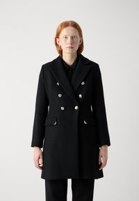 Abrigo negro de doble botonadura en mezcla de lana, con botones plateados, bolsillos laterales y solapa estructurada. Textura suave, ajuste entallado.