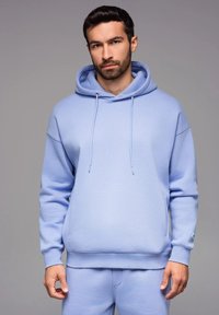 Hoodie bleu clair en tissu doux, avec une capuche à cordon, des poignets côtelés et une poche kangourou. Texture lisse avec un design minimal.