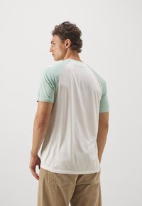 T-shirt leggero con corpo bianco e maniche raglan verde menta. Presenta un collo rotondo e una consistenza del tessuto morbida e liscia.