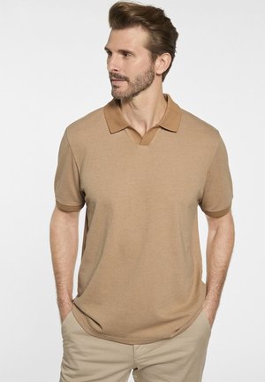 Beige Polohemd mit kurzen Ärmeln und strukturiertem Muster, mit V-Ausschnitt und kontrastierendem Kragen. Kombiniert mit hellbeigen Hosen.