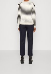 Pull en maille rayé crème et marine, associé à un pantalon marine. Poignets et ourlet côtelés ; détails subtils aux épaules. Bottines à talons épais.